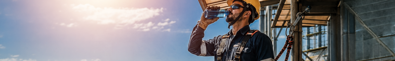 Trabalhador hidratando-se durante pausa à sombra em ambiente industrial, ilustrando prevenção ao estresse térmico